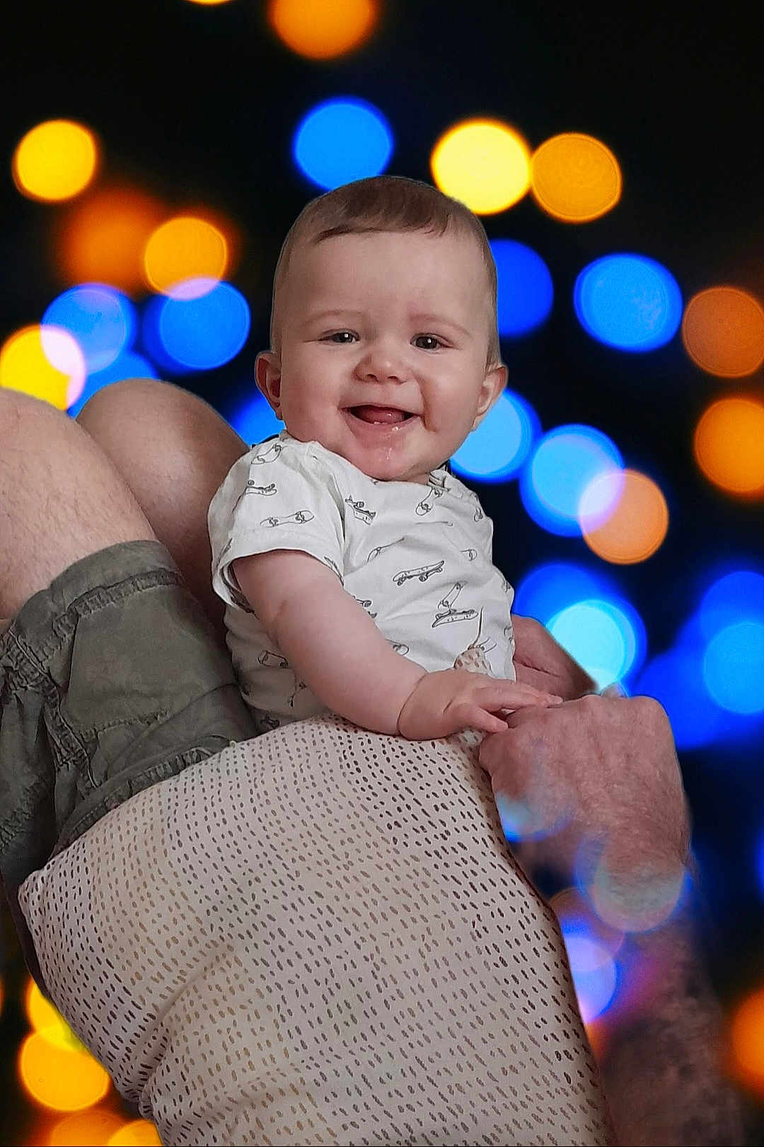 Sasha participe au concours pour gagner de l'argent avec cette photo : baby, child, smile, happy, person, holding, adult, arm, shorts, shirt, pattern, face, skin, head, background, bokeh, lights, colorful, blur, portrait