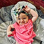 baby, child, smiling, pink_clothing, headband, bow, raising_hand, blanket, indoor, cute, happy, infant, playful, portrait, person, fabric, pattern, skin, toddler, lying_down