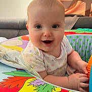 Ellie a rejoint le concours — aidez-le/la à gagner de superbes lots ! apparel, baby, child, closeup, colorful, couch, cute, face, hands, happy, indoor, infant, pattern, person, play_mat, short_sleeve, skin, smiling, soft_toy, toy