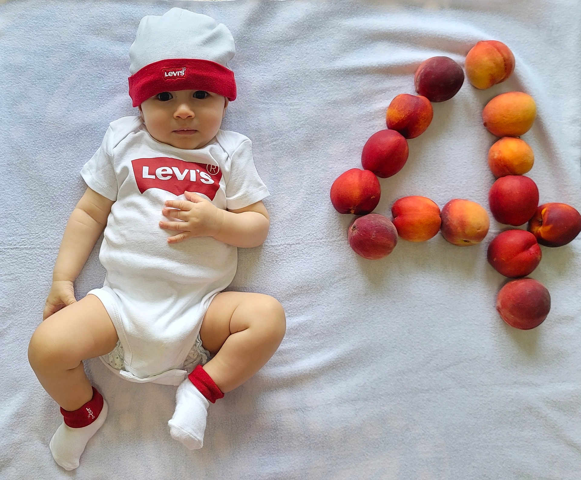 Joud joined the competition — help win amazing prizes! baby, infant, onesie, hat, levi's, peaches, fruit, blanket, white, cute, lying_down, socks, number, playful, soft, indoor, child, portrait, skin, looking