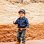 child, toddler, boy, cowboy, hat, cap, denim_shirt, belt, jeans, boots, smiling, standing, outdoor, brick_floor, rustic_wall, portrait, happy, fashion, casual, young_child
