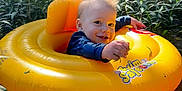 Hudson joined the competition — help win amazing prizes! baby, inflatable_ring, water, pond, greenery, nature, smile, happy, child, outdoor, sunlight, grass, plant, floating, yellow, person, infant, summer, playful, water_plant
