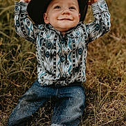 Hudson joined the competition — help win amazing prizes! toddler, child, grass, barefoot, hat, cowboy_hat, jeans, patterned_shirt, smile, outdoor, nature, playful, dirt, happy, sitting, person, portrait, young_child, casual_clothing, daylight