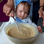 Lyana a rejoint le concours — aidez-le/la à gagner de superbes lots ! toddler, child, baby, adult_hand, whisk, bowl, batter, cooking, kitchen, apron, chef_hat, food_preparation, mixing, high_chair, face, person, clothing, indoor, helping_hand, cute