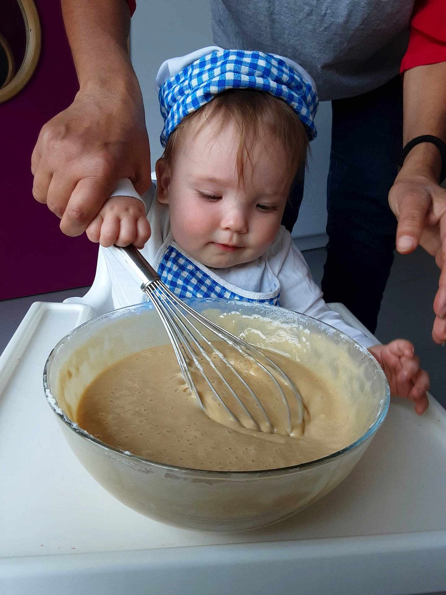Lyana a rejoint le concours — aidez-le/la à gagner de superbes lots ! toddler, child, baby, adult_hand, whisk, bowl, batter, cooking, kitchen, apron, chef_hat, food_preparation, mixing, high_chair, face, person, clothing, indoor, helping_hand, cute