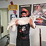Aglaea is registered to the contest to win money with this photo: man, beard, black_cap, black_tshirt, white_cat, long_cat, black_and_white_cat, doorway, horror_posters, indoor, tile_floor, wall_art, tattoos, person, pet, animal, home, funny_pose, cat, holding