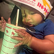 Emiliano joined the competition — help win amazing prizes! baby, child, cup, drink, straw, hand, hat, paper_hat, in_n_out, food_brand, blue_shirt, indoor, curious, close_up, face, portrait, young_child, seated, cute, chubby_cheeks