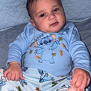 Cesar is registered to the contest to win money with this photo: baby, child, pajamas, blue_clothing, cartoon_character, foot, hand, quilted_background, indoor, cute, infant, sitting, portrait, person, skin, head, face, expression, young_child, comfort