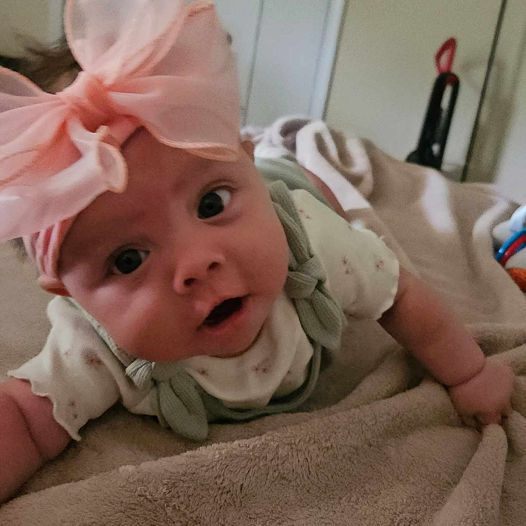 Melody joined the competition — help win amazing prizes! baby, bedroom, blanket, child, close_up, clothing, curious, cute, expression, face, headwear, indoor, infant, lying_down, person, pink_bow, soft_texture, toddler, wide_eyes, young