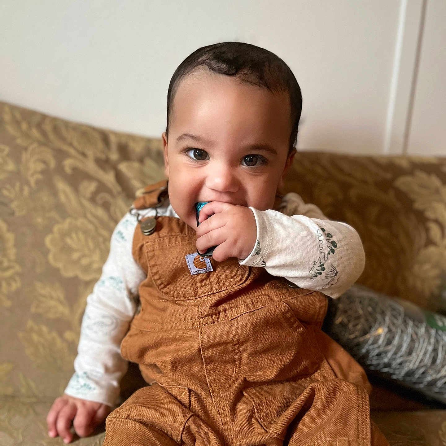 Kaseem joined the competition — help win amazing prizes! baby, brown_clothing, casual_clothing, child, couch, curious, cute, expression, eyes, face, hand, indoor, overalls, patterned_fabric, portrait, sitting, toddler, toy, white_shirt, young_child