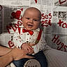 baby, infant, smiling, red_bow_tie, red_suspender, white_shirt, hearts, newspaper_background, handwritten_text, four_months, cute, happy, portrait, child, holding_hand, love, valentine, indoor, person, celebration