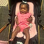 Zuri joined the competition — help win amazing prizes! baby, carrying_item, child, cozy, curly_hair, cushion, cute, floor_mat, footwear_free, furniture, happy, indoor, infant, person, pink_clothing, portrait, seated, smiling, stroller, wallet