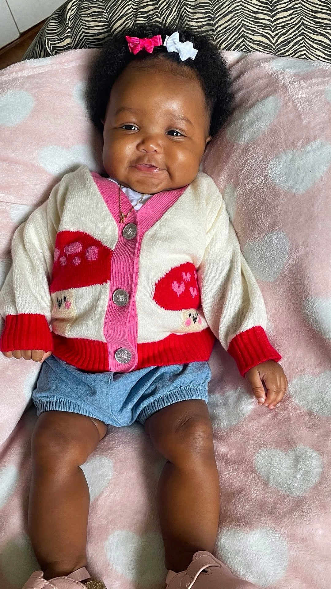Reagan is registered to the contest to win money with this photo: baby, infant, child, smiling, hair_bows, cardigan, mushroom_pattern, denim_shorts, pink_blanket, heart_pattern, cute, lying_down, soft_texture, cheeks, skin, hand, legs, shoes, indoors, portrait