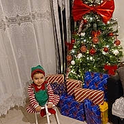 Jean-Joseph a rejoint le concours — aidez-le/la à gagner de superbes lots ! child, toddler, christmas_tree, presents, wrapped_presents, giant_bow, ornaments, string_lights, rocking_horse, pajamas, elf_costume, smile, curtains, floor_tiles, sofa, holiday_decor, indoor, festive, gift_wrap, cozy