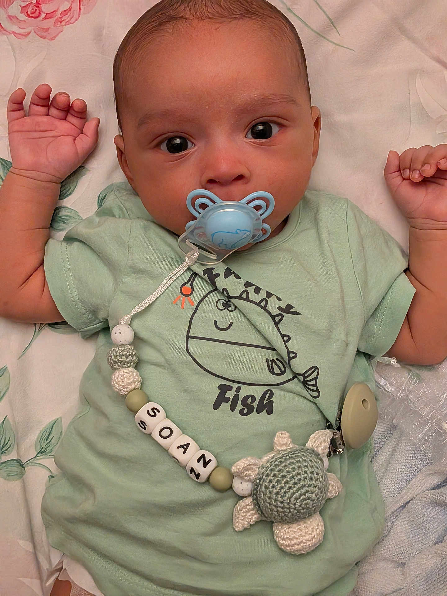 Soan a rejoint le concours — aidez-le/la à gagner de superbes lots ! baby, pacifier, shirt, fish_graphic, toy, knitted_turtle, lying_down, curious, calm, infant, child, bed, bedding, pastel_colors, hand, face, cute, soft, indoors, sleepwear