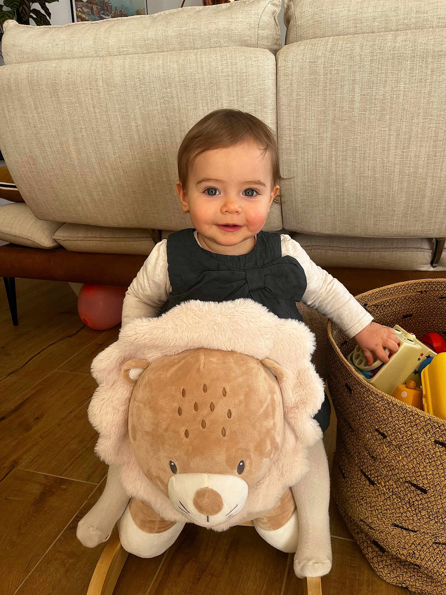Mia participe au concours pour gagner de l'argent avec cette photo : toddler, child, baby, plush_lion, rocking_toy, sofa, couch, basket, toys, wooden_floor, smile, indoor, living_room, dress, bow, stuffed_animal, playtime, cheeks, eyes, hand