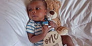 Taige is registered to the contest to win money with this photo: baby, bed, child, comfort, cozy, cute, face, hand, indoor, infant, lying_down, newborn, onesie, portrait, skin, soft_toys, striped_clothing, teddy_bear, white_bed, wooden_sign