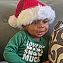 Taige is registered to the contest to win money with this photo: toddler, child, santa_hat, green_shirt, couch, pillow, indoors, holiday, festive, cute, smiling, portrait, cozy, happy, young_child, clothing, sitting, face, person, home
