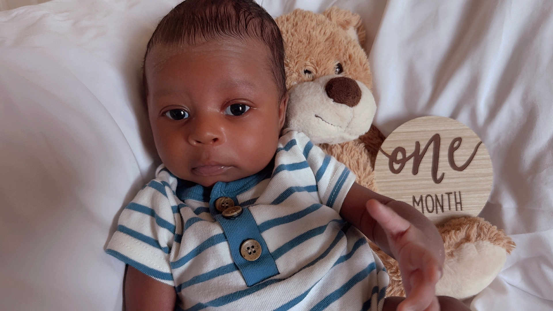 Taige is registered to the contest to win money with this photo: baby, child, cozy, cute, face, hand, indoors, infant, milestone, newborn, one_month, plush_toy, portrait, smiling, soft_lighting, striped_onesie, teddy_bear, white_blanket, wooden_sign, young