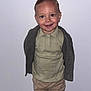 toddler, child, boy, standing, smiling, polo_shirt, cardigan, pants, indoor, portrait, hairstyle, neat, confident, white_wall, casual_clothing, cute, young_child, fashion, person, human