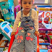 Legna is registered to the contest to win money with this photo: child, girl, denim_overalls, white_shirt, pink_bows, slide, playroom, toys, colorful, indoor, floor_mat, sneakers, expressionless, young_child, window_ac, plastic_toys, play_area, casual_clothing, kid, portrait