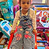 child, girl, denim_overalls, white_shirt, pink_bows, slide, playroom, toys, colorful, indoor, floor_mat, sneakers, expressionless, young_child, window_ac, plastic_toys, play_area, casual_clothing, kid, portrait