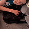 person, sleeping, bed, black_cat, cat, hugging, cozy, indoor, pillow, blanket, resting, animal, pet, relaxing, comfort, human, feline, close_up, casual_clothing, peaceful