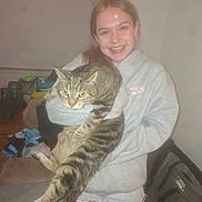 Dr Sheldon.l.cooper is registered to the contest to win money with this photo: girl, smile, cat, tabby_cat, hoodie, denim_shorts, indoor, person, pet, animal, happy, cute, casual, home, furniture, living_room, holding, long_tail, young, braces