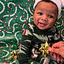 baby, child, smiling, santa_hat, holiday, christmas, gift_bow, festive, pajamas, green_background, tattooed_hand, sitting, happy, cute, portrait, celebration, indoors, decor, colorful, fun