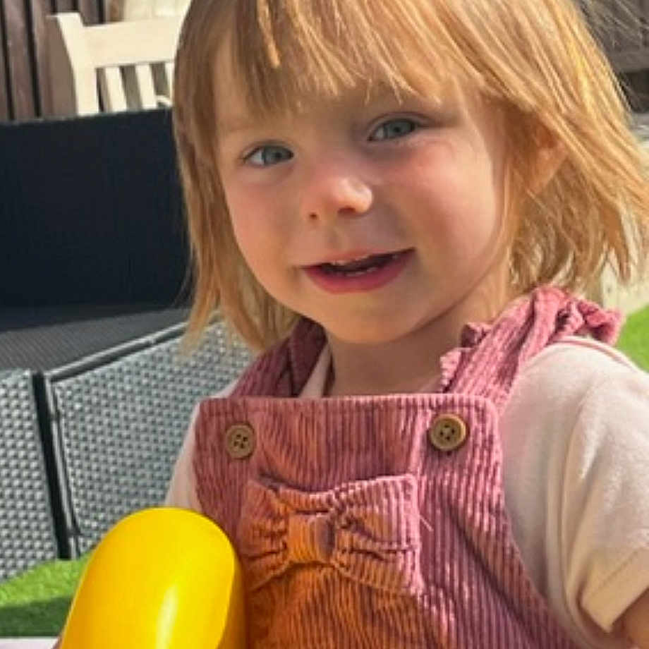 Gabriella is registered to the contest to win money with this photo: banana, child, clothing, couch, face, female, food, fruit, furniture, girl, grass, head, outdoors, pants, person, photography, plant, playarea, portrait, produce