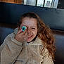 child, girl, curly_hair, smiling, laughing, beige_jacket, fleece, indoor, window, playful, hand, face, brown_hair, seat, casual_clothing, young, portrait, fun, happy, light