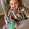 Azrah is registered to the contest to win money with this photo: child, toddler, baby, highchair, tray, suction_toy, toy_wheel, plaid_shirt, harness, smiling, laughing, curly_hair, seat, indoor, wall, carpet, portrait, candid, happy, clothing