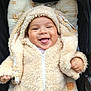 baby, smiling, tongue_out, hoodie, fluffy_clothing, infant, cute, cushion, patterned_textile, seated, happy, child, warm_clothing, indoors, closeup, face, young_child, cozy, apparel, zipped_jacket