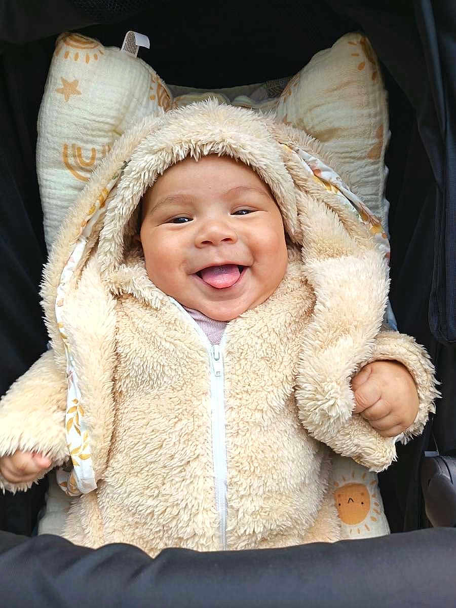Kaelan a rejoint le concours — aidez-le/la à gagner de superbes lots ! baby, smiling, tongue_out, hoodie, fluffy_clothing, infant, cute, cushion, patterned_textile, seated, happy, child, warm_clothing, indoors, closeup, face, young_child, cozy, apparel, zipped_jacket