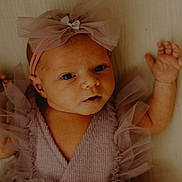 Ella joined the competition — help win amazing prizes! baby, infant, child, face, headband, bow, dress, purple, tulle, clothing, cute, portrait, newborn, skin, hands, eyes, lying_down, soft_light, indoors, expression