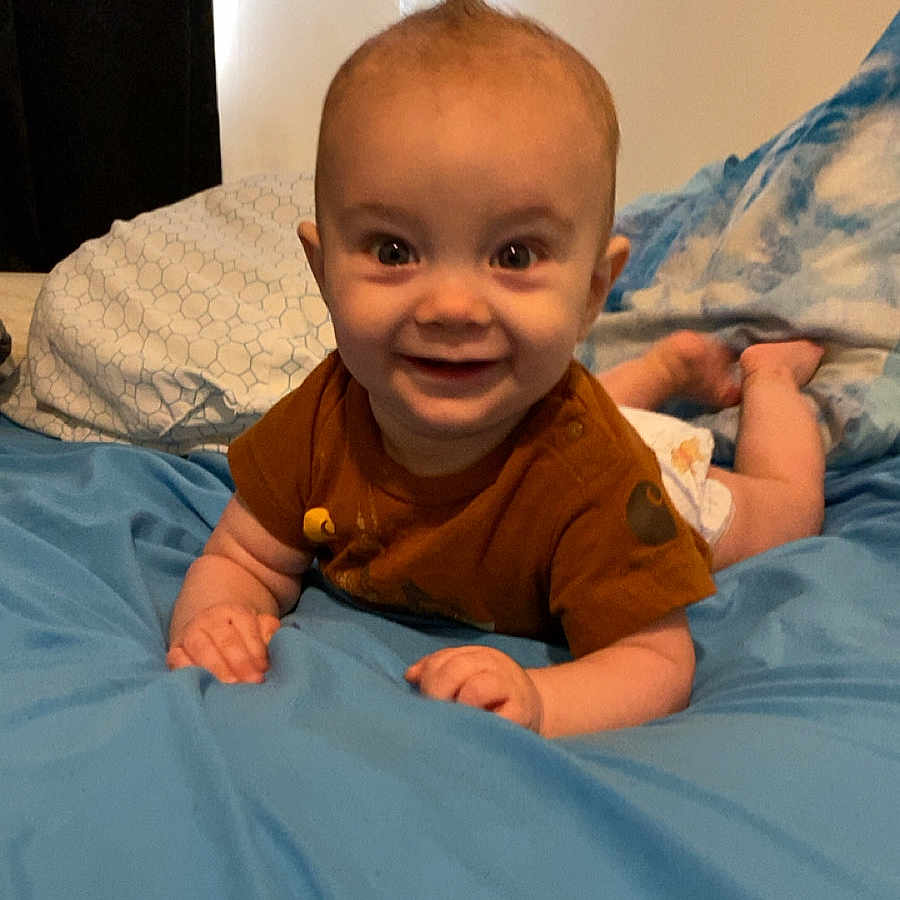 Phoenix is registered to the contest to win money with this photo: baby, bed, blanket, blue, brown, child, clothing, cute, diaper, face, hair, happy, indoors, lying_down, mohawk, person, pillow, skin, smiling, toddler