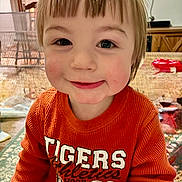 Walker is registered to the contest to win money with this photo: child, toddler, smiling, indoor, sweater, orange_clothing, face, hair, portrait, person, home, furniture, table, toy, cheeks, cute, happy, young, casual, clothing