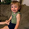 Walker is registered to the contest to win money with this photo: toddler, child, smiling, couch, indoor, green_tank_top, shorts, plant, curtain, brown_couch, happy, boy, face, hair, skin, furniture, relaxing, home, portrait, casual