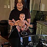 baby, child, person, smile, kitchen, motorcycle, handlebars, windshield, indoor, cabinet, countertop, door, trash_can, light_switch, tattoo, short_sleeve_shirt, floor, expression, holding, curtain
