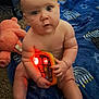 baby, child, toy, blanket, carpet, plush_toy, teddy_bear, playpen, indoor, floor, sitting, naked, face, hands, feet, light, red_light, blue_blanket, menorah_pattern, star_pattern