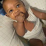 Cairo is registered to the contest to win money with this photo: baby, infant, child, face, hand, sock, pillow, striped_clothing, chewing, curious, indoors, cute, young_child, skin, person, portrait, sitting, comfort, blanket, resting