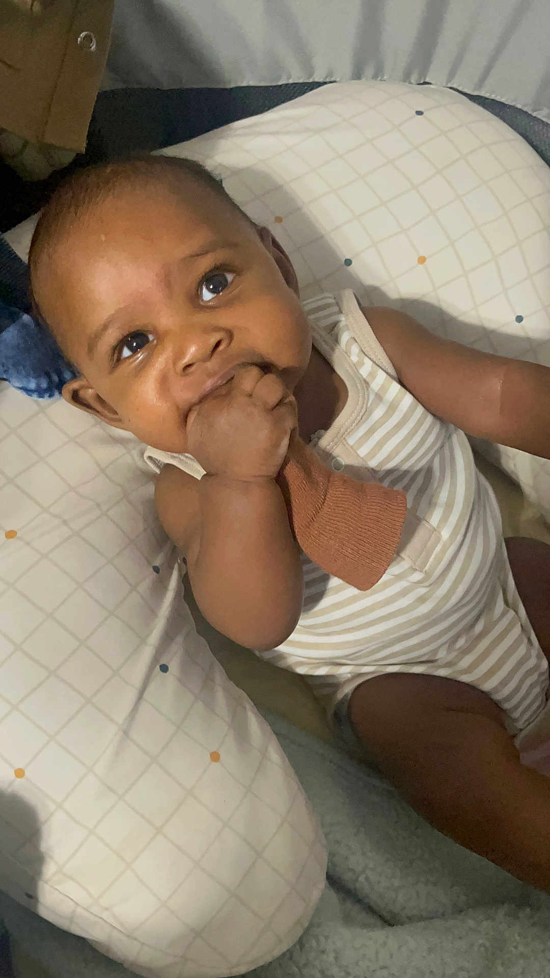 Cairo is registered to the contest to win money with this photo: baby, infant, child, face, hand, sock, pillow, striped_clothing, chewing, curious, indoors, cute, young_child, skin, person, portrait, sitting, comfort, blanket, resting