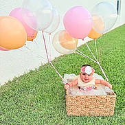 Allyson joined the competition — help win amazing prizes! baby, basket, balloon, grass, flower_headband, outdoor, child, smiling, dress, pastel_colors, greenery, happy, cute, celebration, wicker, toddler, nature, fun, portrait, playful