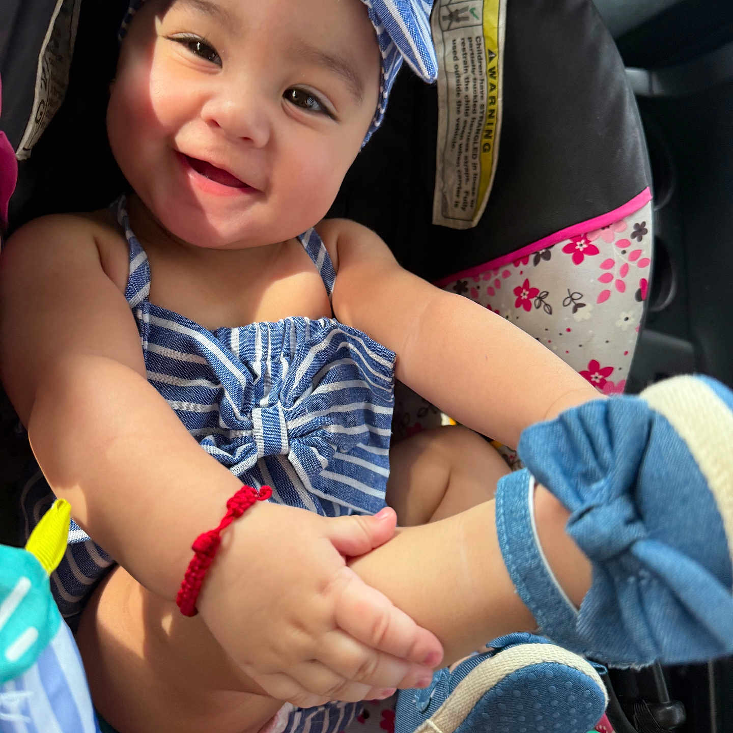 Allyson is registered to the contest to win money with this photo: baby, baby_shoes, blue_striped_clothing, car_seat, child, cute, floral_pattern, footwear, happy, headband, indoors, infant, people, playful, portrait, red_bracelet, seat, seatbelt, smiling, toddler