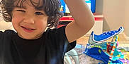Jairon is registered to the contest to win money with this photo: black_shirt, carpet, child, curly_hair, curtain, fun, furniture, gesture, happy, home, indoor, kid, living_room, orange_shorts, person, playful, smile, television, toys, young