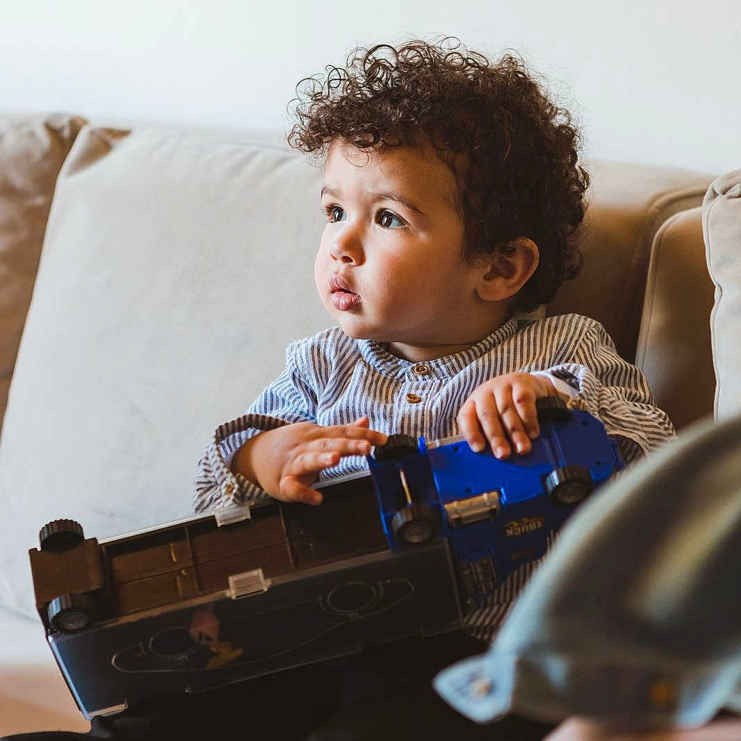 Hedi participe au concours pour gagner de l'argent avec cette photo : baby, camera, clothing, couch, curlyhair, e_scooter, electronics, face, furniture, gun, hair, head, person, photography, portrait, sitting, transportation, vehicle, videogaming, weapon