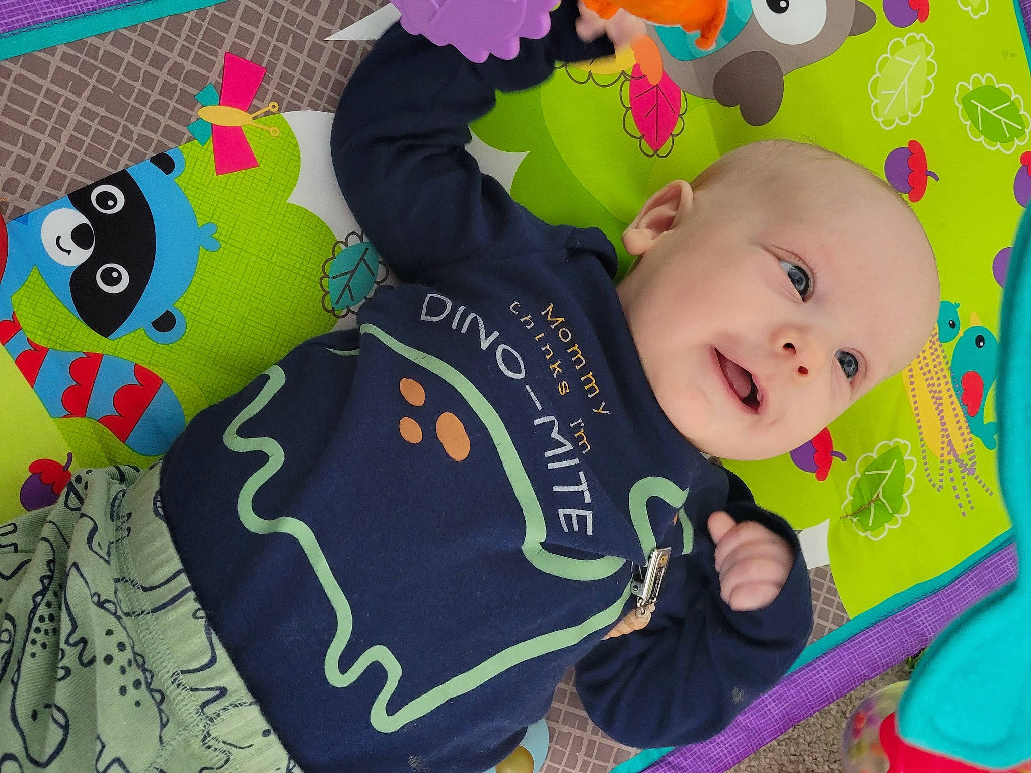 Ridge is registered to the contest to win money with this photo: baby, baby_products, baby_toddler_clothing, baby_toys, cheek, child, flooring, font, green, happy, linens, pattern, person, play, sleeve, smile, stuffed_toy, t_shirt, textile, toddler