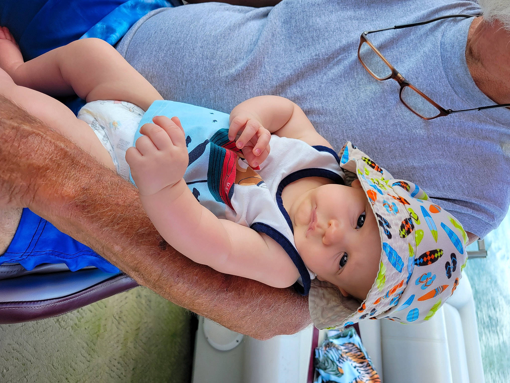 Ridge is registered to the contest to win money with this photo: arm, azure, baby, baby_toddler_clothing, blue, comfort, eye, facial_expression, finger, gesture, glasses, hand, happy, hat, headwear, human_body, joint, leg, organ, person