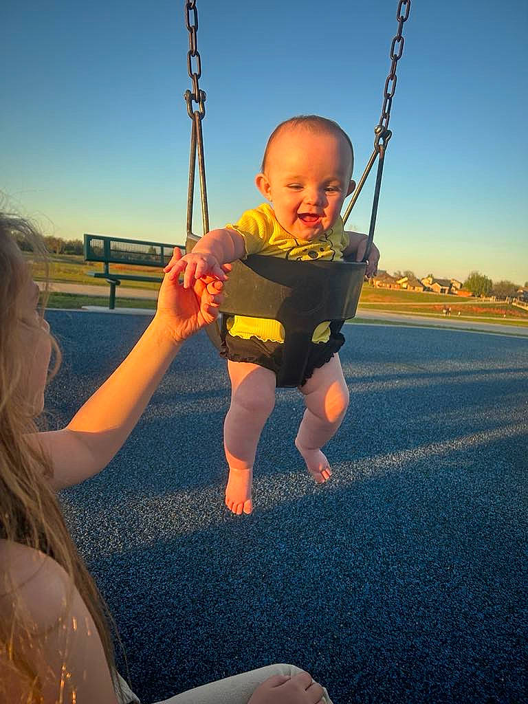 Delilah is registered to the contest to win money with this photo: arm, elbow, finger, fun, gesture, grass, hand, happy, human_body, leg, leisure, outdoor_play_equipment, people_in_nature, person, playground, recreation, sky, smile, swing, thumb