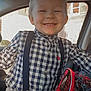 child, smiling, blond_hair, checkered_shirt, suspenders, denim_jeans, car_interior, backpack, spiderman, window, building, seatbelt, happy, casual_clothing, young, portrait, indoors, seat, buttoned_shirt, light
